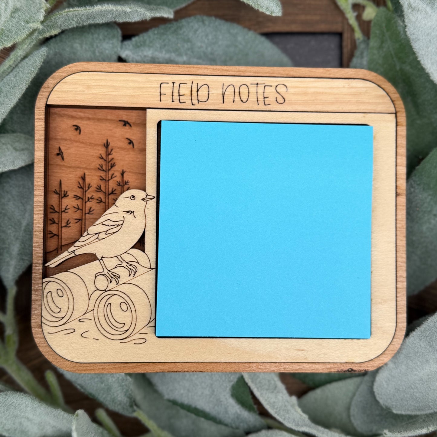 Wooden notebook cover with bird illustration and 'Field Notes' branding on a green leaf background