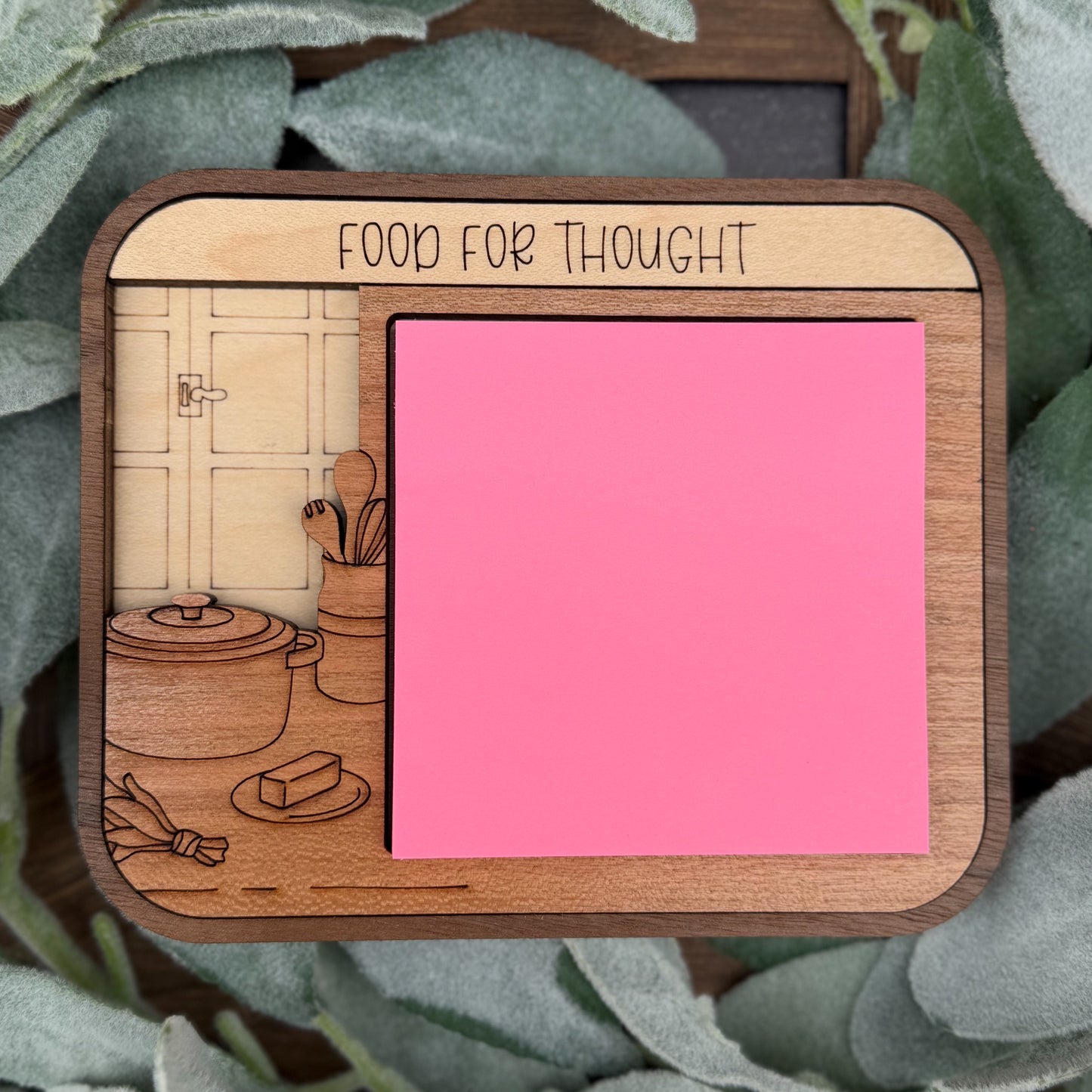 Wooden notepad with pink surface and decorative illustrations on a leafy background