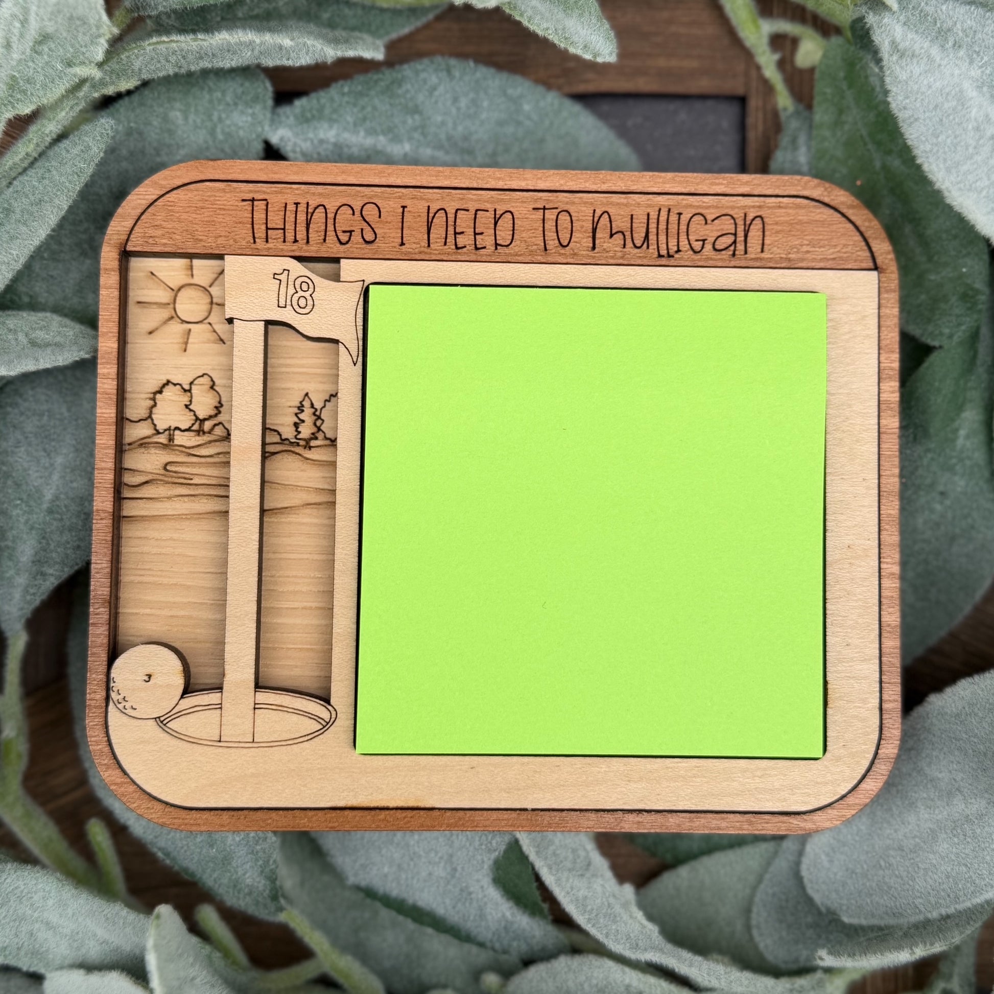 Wooden memo board with green sticky notes and engraved designs on a leafy background