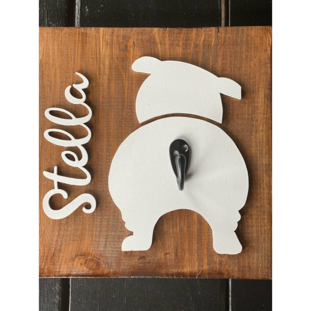 Wooden dog leash holder with white bulldog silhouette, personalized name “Stella,” and black metal hook on rustic wood background.
