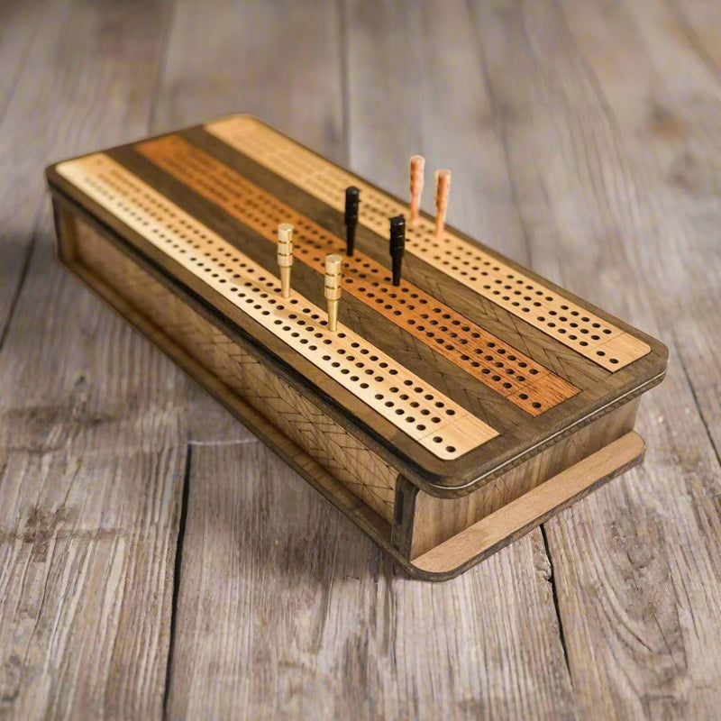 Laser cut wooden cribbage board with striped hardwood design and metal pegs on marble background.