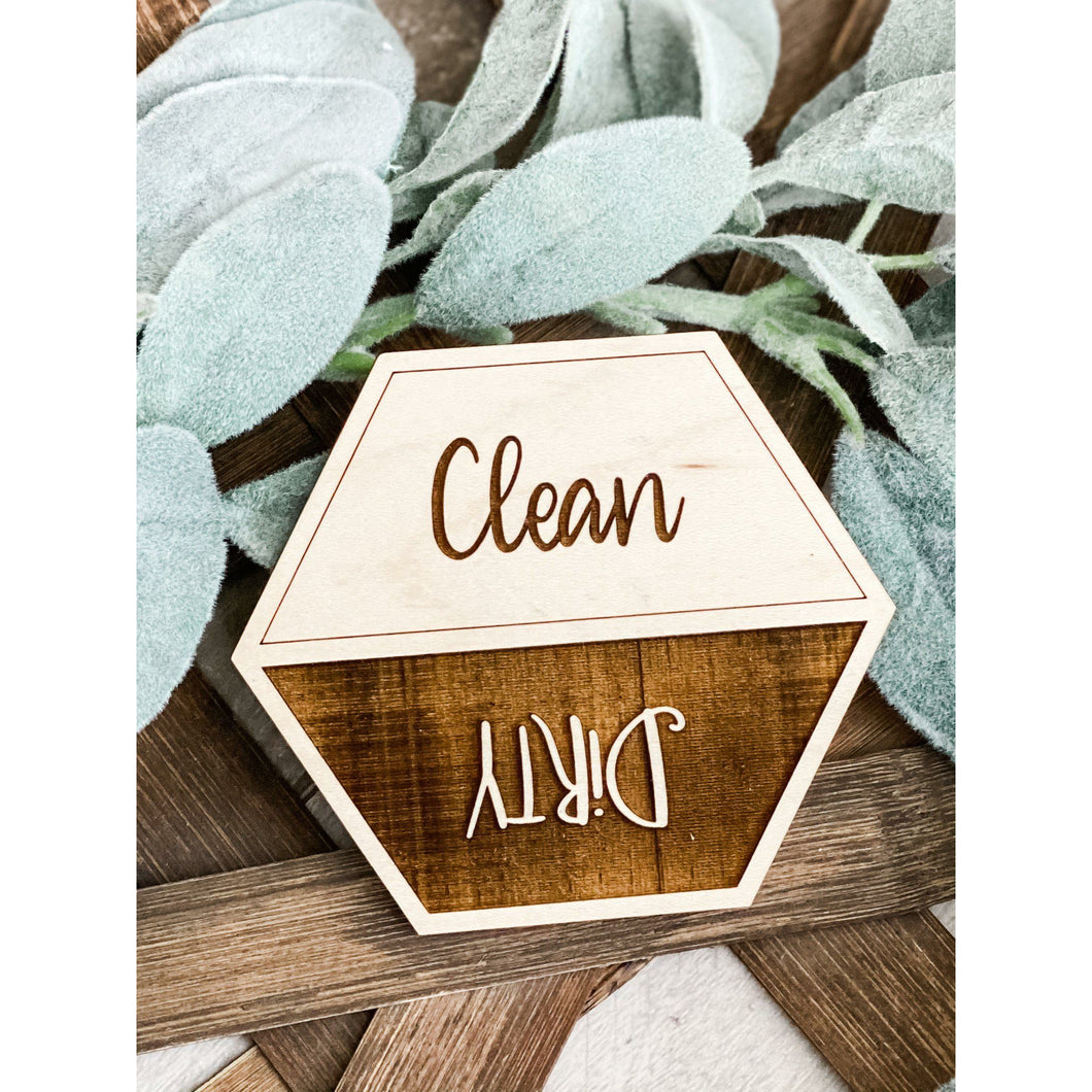 Wooden dishwasher magnet with “Clean” on one side and “Dirty” on the other, placed on rustic background with greenery accents.