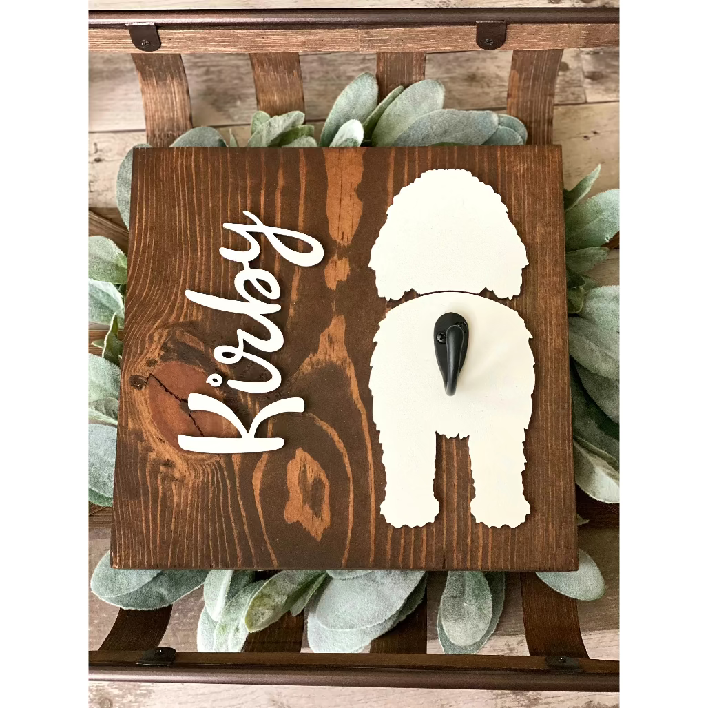 Wooden dog leash holder with white doodle silhouette, personalized name “Kirby,” and black metal hook on rustic wood background.