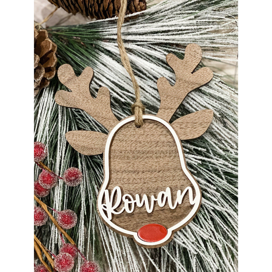Wooden reindeer ornament with red nose and personalized name displayed on frosted pine branches with red berries.