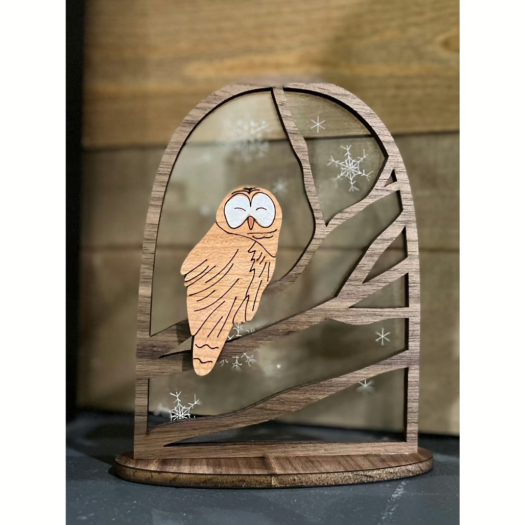 A wooden standing sign featuring an owl perched on a branch with snowflake accents and a laser-cut design.